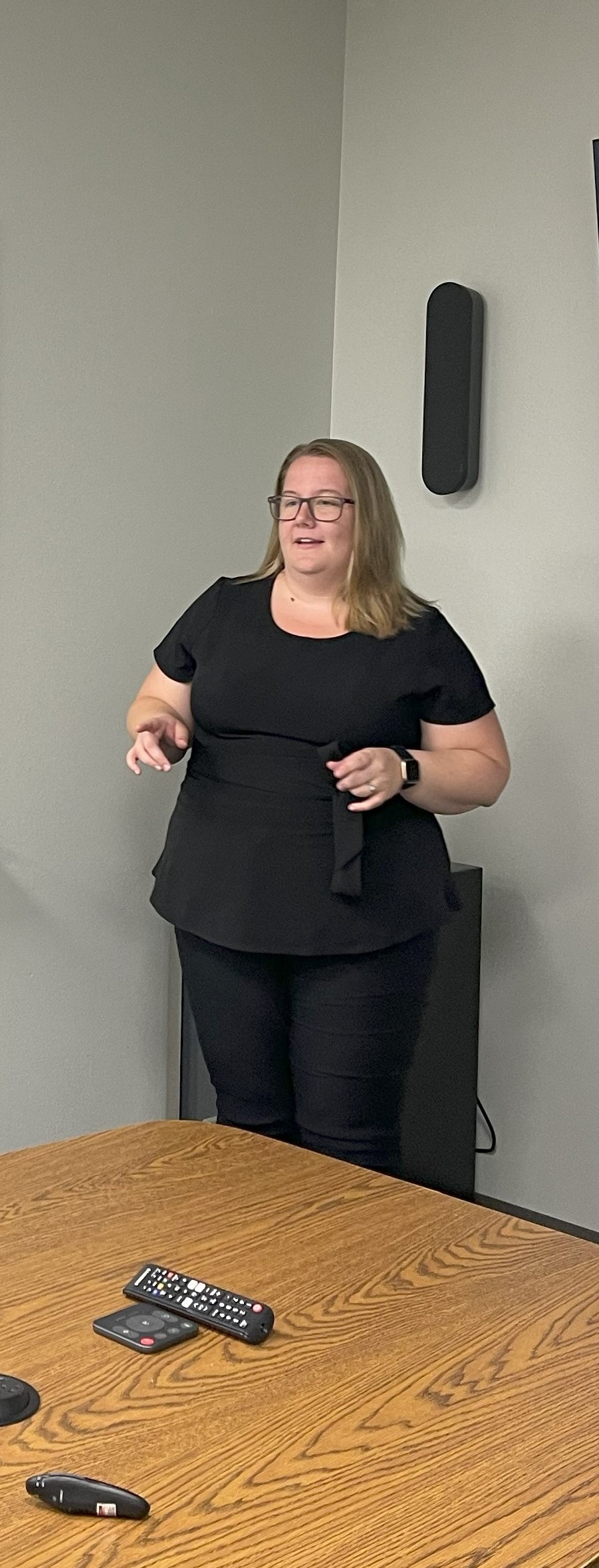 Stephanie Kunkel hosts a team building event in a board room, she stands in the corner near a white board she's dressed in black, her hands spread at her waist as she obviously discusses an important topic with the leaders in the room, she has blonde, shoulder length hair, dark glasses and a slight smile. She continues to shift perspectives.