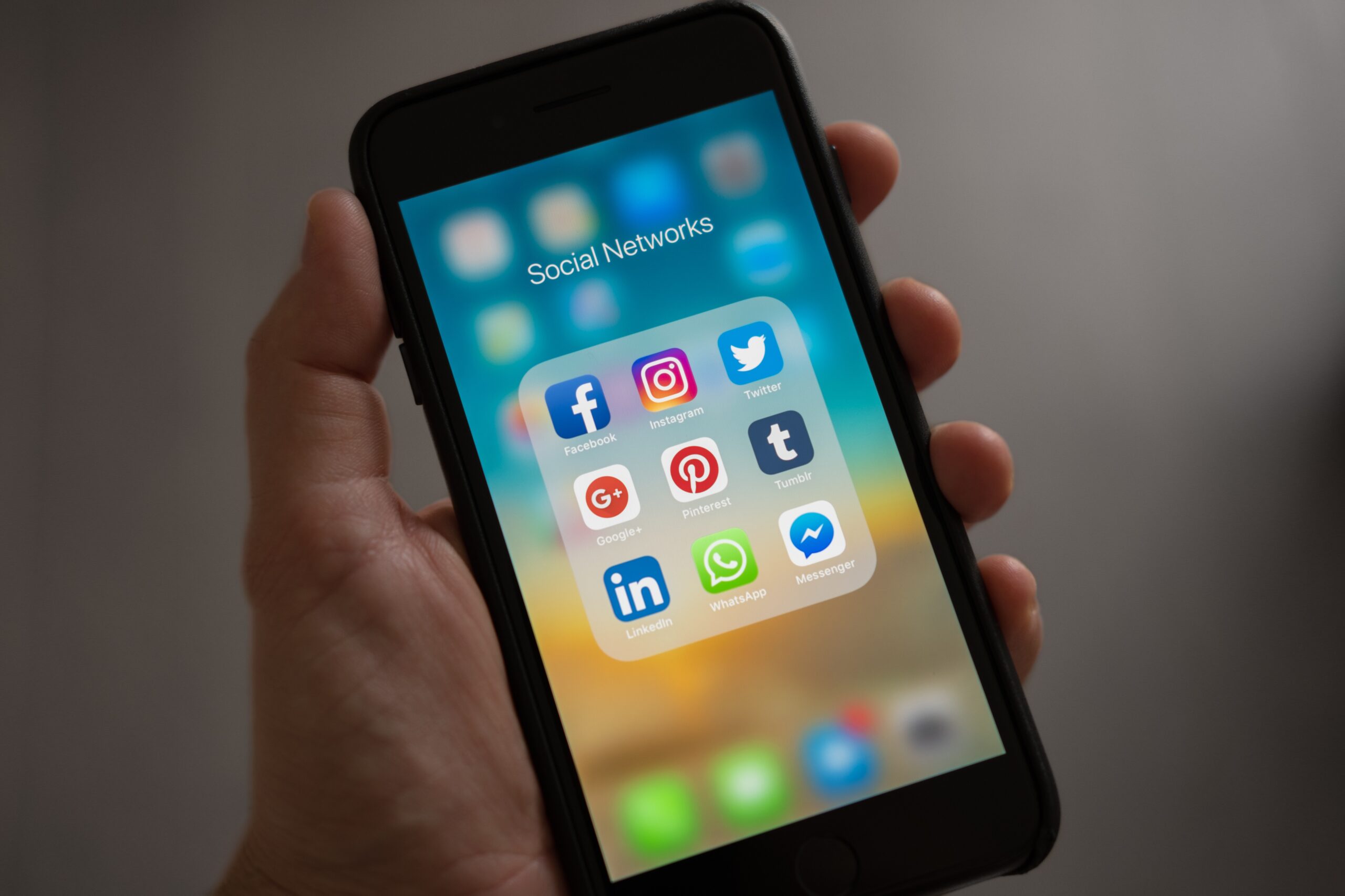 A hand holding a smartphone displaying a folder labeled Social Networks with apps including Facebook, Instagram, Twitter, and others on the screen. Get mental health Coaching When you need it through voxer.