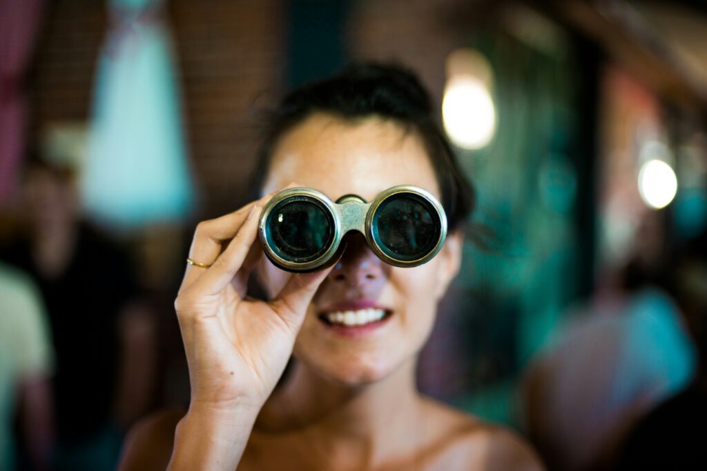 A person, smiling through a pair of vintage binoculars, surrenders to the moment. The background is blurred with dim lighting, adding an aura of mystery and power.